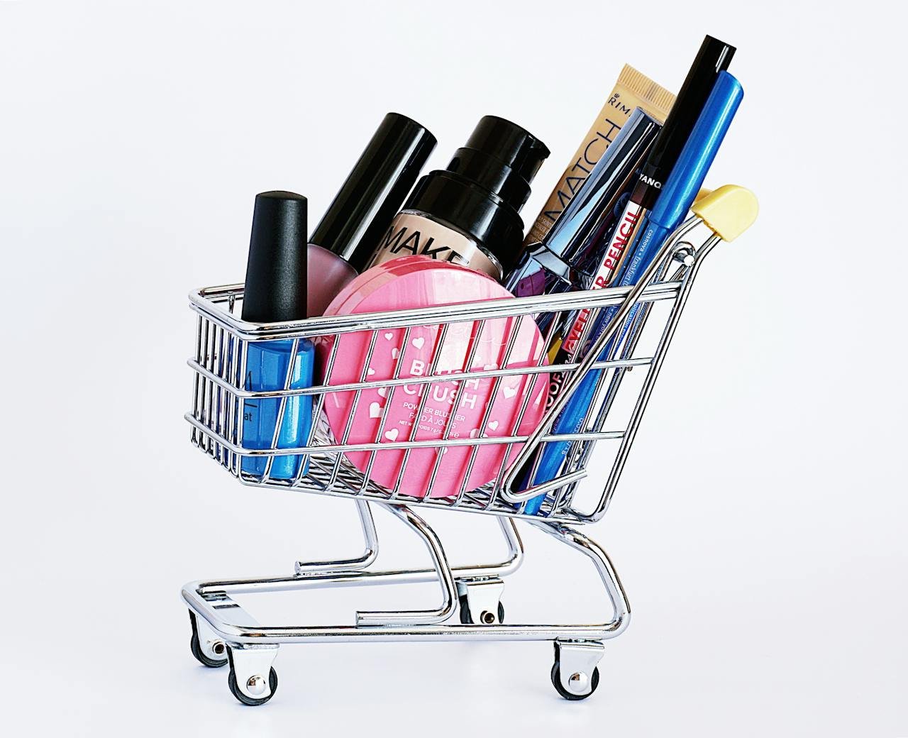 creative-03 Miniature shopping cart filled with a variety of cosmetics on a white background.