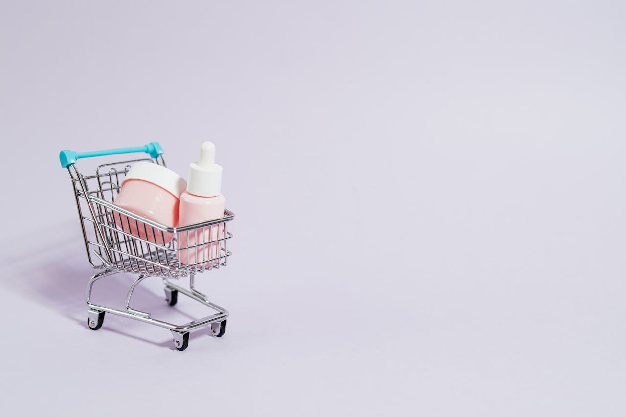 creative-02 Small shopping cart holding pink skincare products on a pastel background.