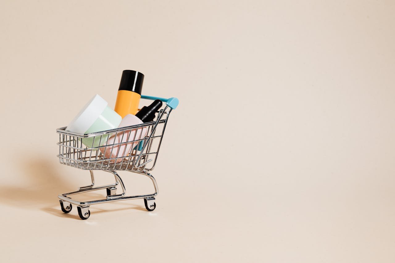 mobile-01 A minimalist image of a mini shopping cart filled with cosmetics on a beige background, ideal for e-commerce concepts.