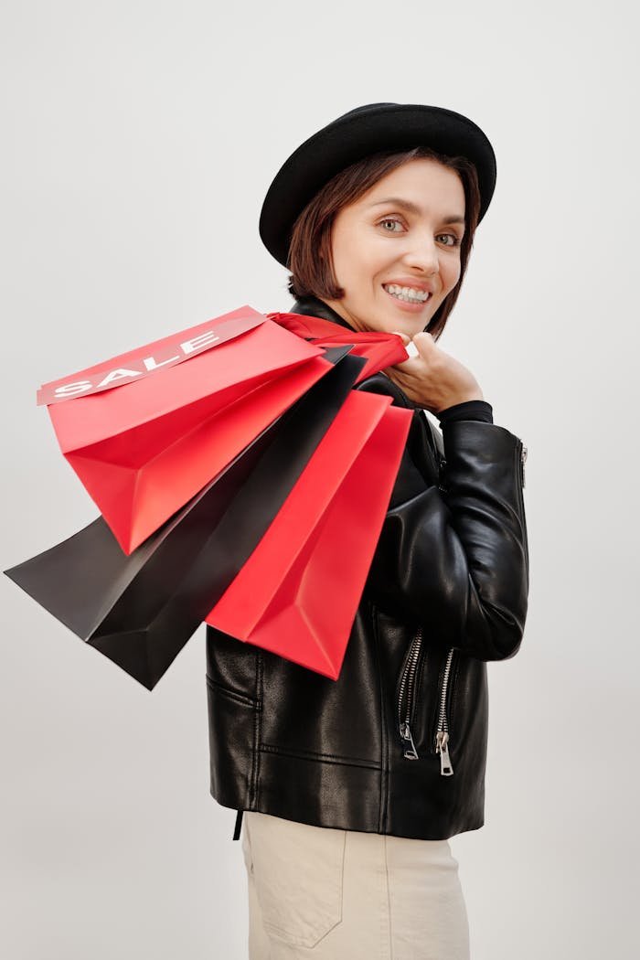 brand-01 Smiling woman in black hat holding red and black sale shopping bags, representing modern consumerism.