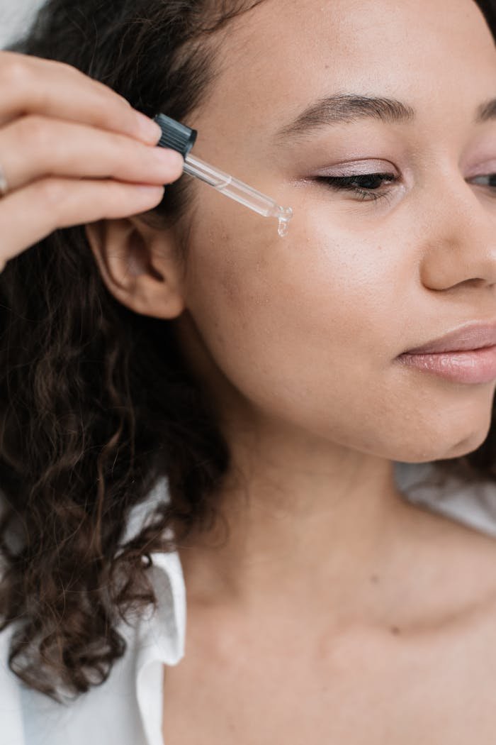 digital-01 A young woman applying skincare serum to her face with a dropper for a beauty treatment.